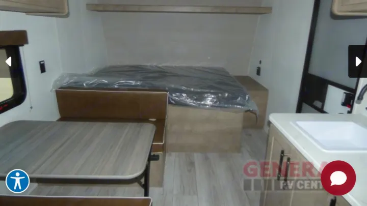 Spacious RV rental interior features a cozy bed, convertible dinette, and compact kitchen sink area.. Keystone Springdale 2025