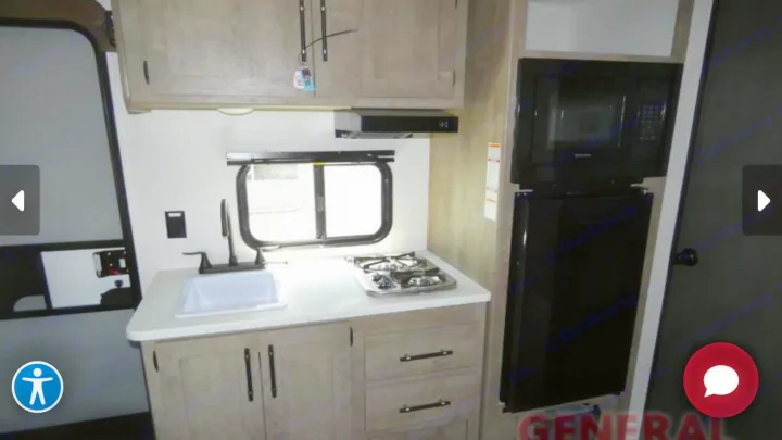 Interior view of an RV rental kitchen showing a sink, stovetop, range hood, microwave, fridge, and wood cabinets.. Keystone Springdale 2025