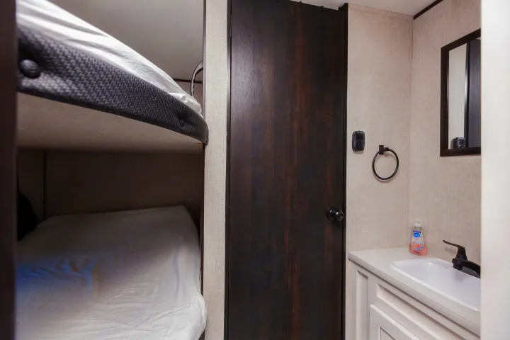 Compact RV rental interior featuring bunk beds, a dark door, and a small bathroom vanity with sink.. Jayco Jay Flight SLX 2024