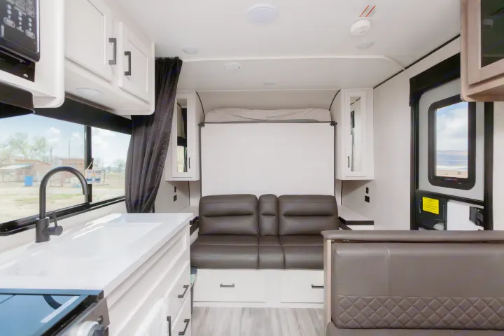 RV rental interior: a modern kitchen with sink and a comfy living area featuring a sofa and pull-down bed.. Jayco Jay Flight SLX 2024