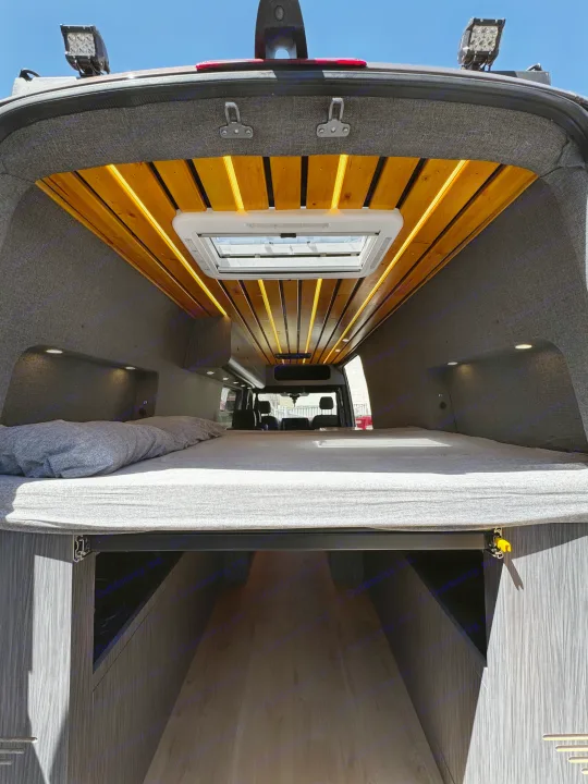 Spacious custom RV rental interior features a cozy bed, ample storage, and stylish wood ceiling with lighting.. Mercedes-Benz Sprinter 2023