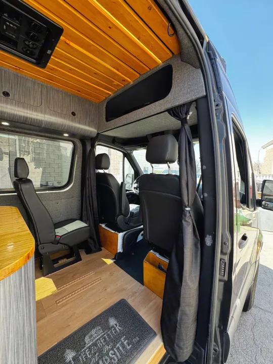 Interior of a custom RV rental camper van featuring a warm wood ceiling, modern grey walls, flexible seating, and hardwood floors.. Mercedes-Benz Sprinter 2023