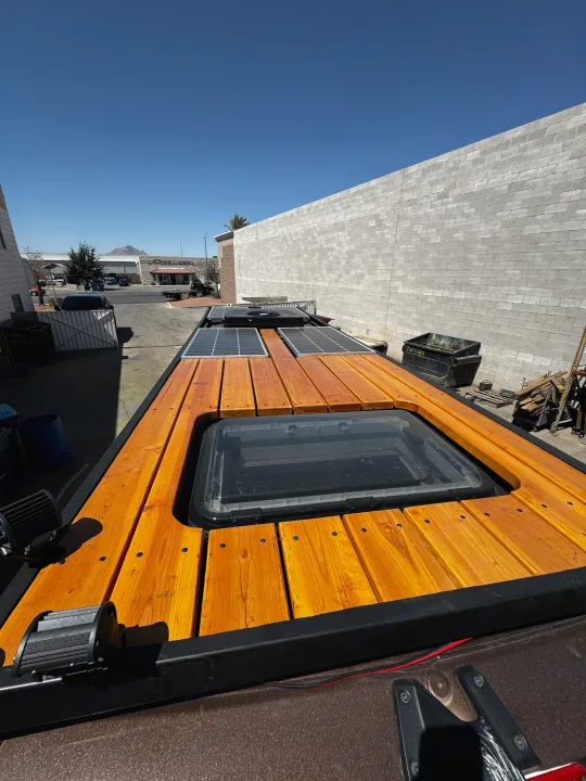 Top-down view of an RV rental roof featuring a wooden deck, skylight, and solar panels for off-grid adventures.. Mercedes-Benz Sprinter 2023