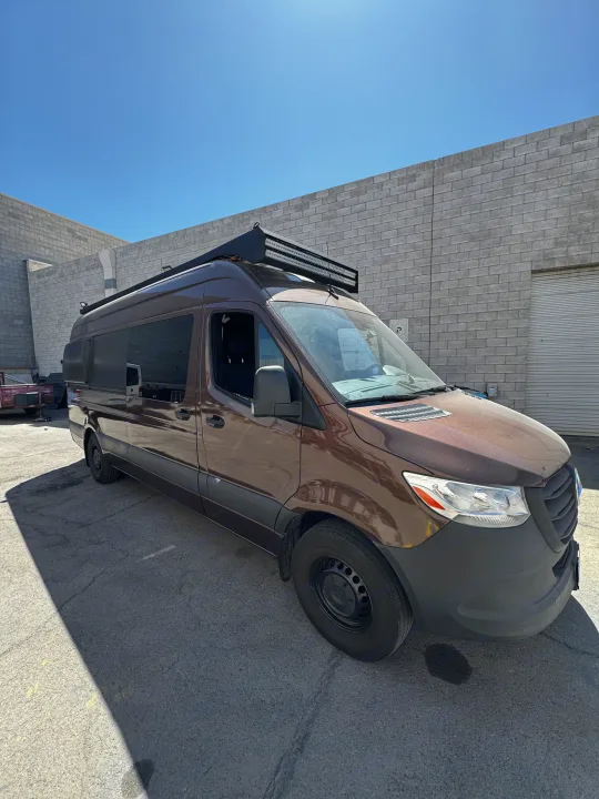 Brown Sprinter camper van, ideal for RV rental, parked outside a building under a clear blue sky.. Mercedes-Benz Sprinter 2023