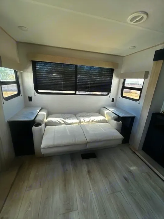 Clean RV rental interior: sofa bed, side tables, large windows with blinds, and light wood floors.. Primetime Avenger 2025