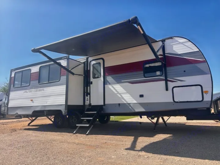 White RV rental travel trailer setup for outdoor living, featuring an extended awning & entry steps. Ready for adventure!. Primetime Avenger 2025
