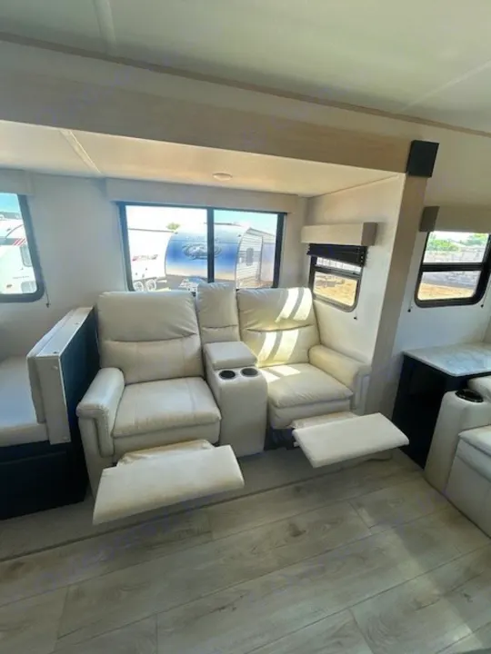Comfortable RV rental interior with dual recliners, extended footrests, cup holders, and light wood flooring.. Primetime Avenger 2025