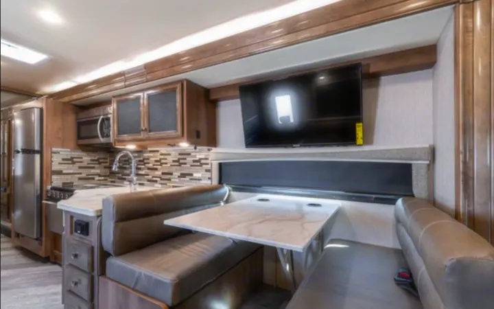 Spacious RV rental interior featuring a modern kitchen, dinette, and TV setup for comfortable travels.. Holiday Rambler Invicta 2021