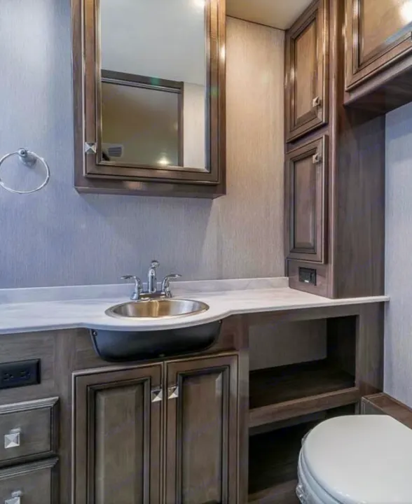 This RV rental's modern bathroom features a sleek vanity, sink, mirror, toilet, and ample storage cabinets. Travel in comfort!. Holiday Rambler Invicta 2021