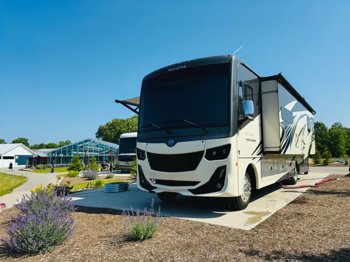 A modern Invicta Class A RV rental is perfectly parked on a sunny day at a well-maintained resort campground.. Holiday Rambler Invicta 2021