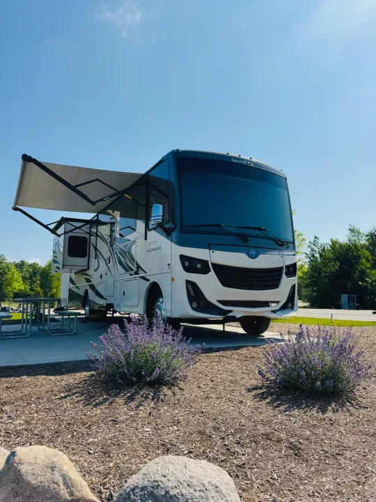 Holiday Rambler Invicta rv rental at a sunny campsite, showcasing its extended awning and slide-outs.. Holiday Rambler Invicta 2021