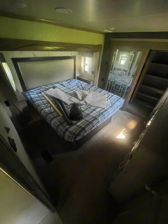 RV rental bedroom with a plaid bed, light from a window, and a mirrored doorway revealing another area. Cozy mobile living space.. Cedar Creek Champagne 2019