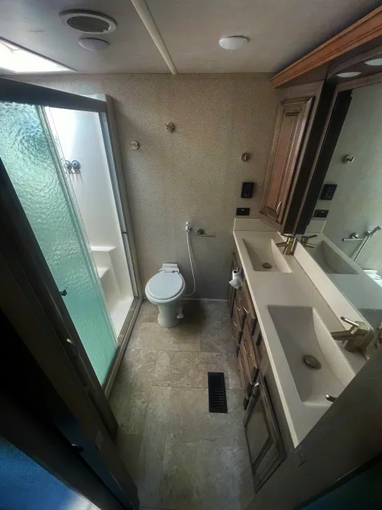 Full RV rental bathroom with glass shower, toilet (bidet sprayer), and dual sink vanity, offering a complete and clean space.. Cedar Creek Champagne 2019