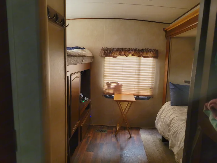 RV rental interior: compact bedroom with bunk and main beds, window, wood floor, & portable table.. Forest River Wildwood Heritage Glen Lite 2014