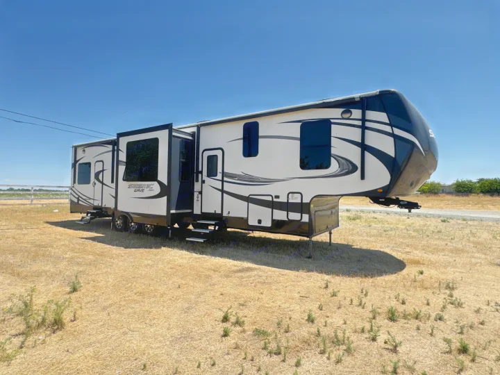 Spacious Jayco Seismic Wave fifth-wheel RV rental parked on dry grass under a blue sky, ready for adventure.. Jayco Seismic Toy Hauler 2017