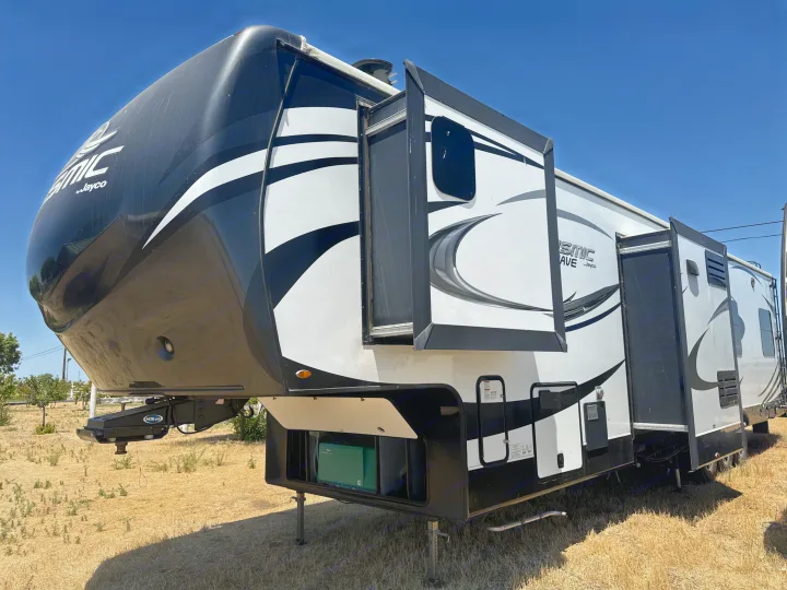 Large black & white fifth-wheel RV, with slides extended, parked in dry grass under blue sky. Ideal for RV rental.. Jayco Seismic Toy Hauler 2017
