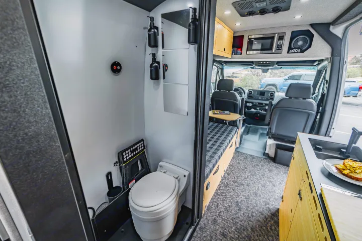RV rental interior featuring a compact wet bath with toilet and shower, kitchen with sink, and a convertible sleeping area.. Mercedes Sprinter 2023