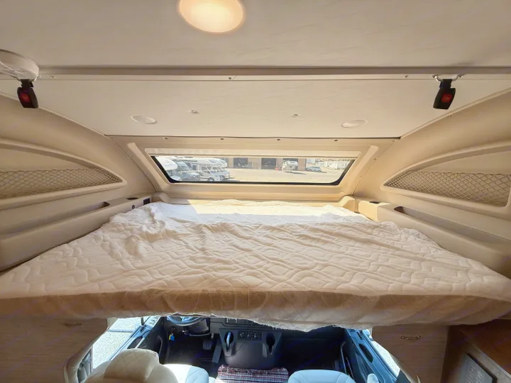 Spacious cab-over bed in this RV rental, featuring built-in storage nets and the view from above the driver's cab.. Jayco Seneca 2025