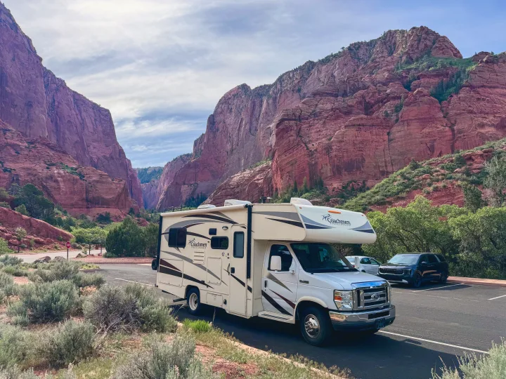 RV rental parked in a dramatic red rock canyon, featuring towering cliffs and lush greenery, perfect for national park travel.. Coachmen Freelander 21QB 2016