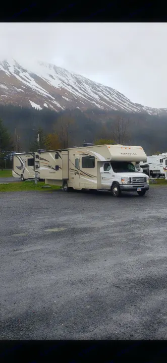 Two RVs on a wet gravel lot with snow-capped mountains. An RV rental is ideal for exploring such scenic outdoor destinations.. Winnebago Minnie Winnie 2017