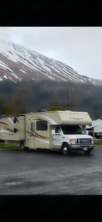 Beige Winnebago rv rental with slide-out extended, parked on gravel, backed by snowy mountains.. Winnebago Minnie Winnie 2017