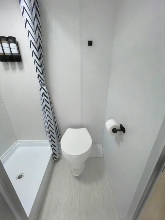 Modern compact RV rental bathroom: white toilet, shower with chevron curtain, amenities dispenser, and TP holder.. Forest River Salem 2024