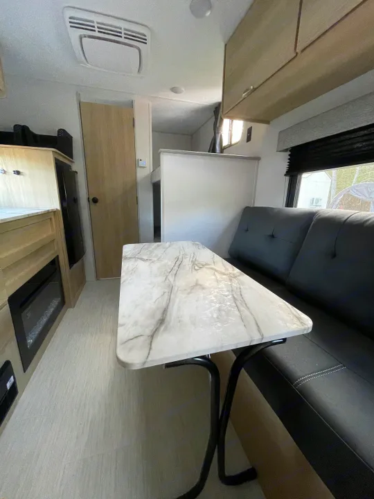 RV rental interior: modern dining area with marble-look table, dark bench seating, fireplace, and overhead cabinets.. Forest River Salem 2024