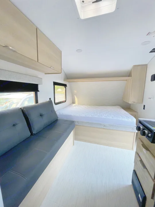 Modern RV rental interior featuring a cozy bed, black sofa, light wood cabinetry, and compact kitchenette.. Forest River Salem 2024