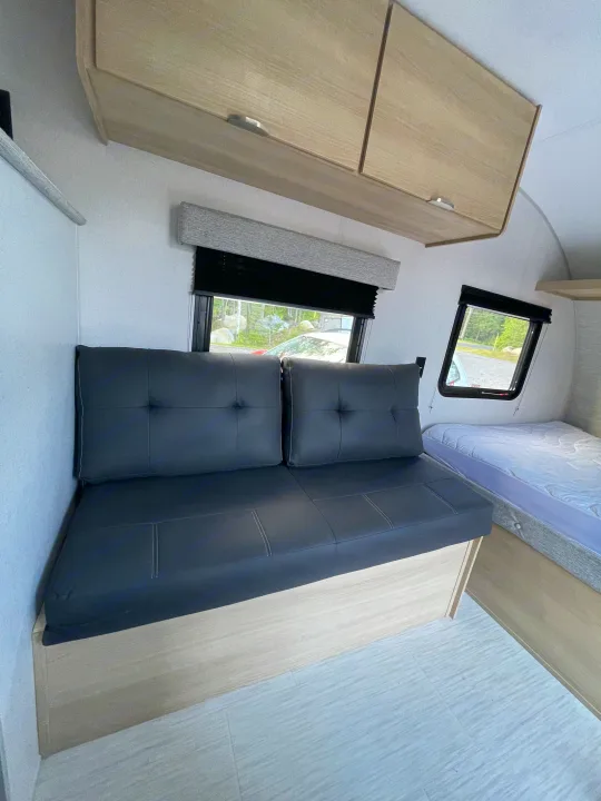 RV rental interior with a black futon sofa, light wood cabinets, and a bed. Bright and modern camper space.. Forest River Salem 2024
