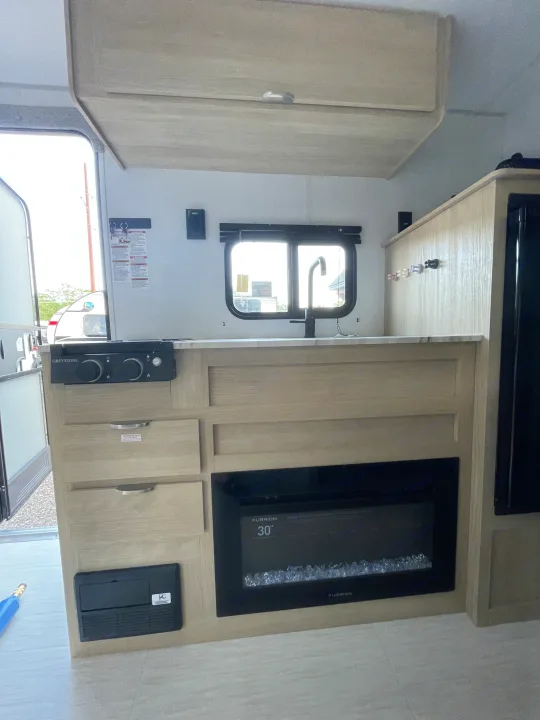 Cozy RV rental interior with light wood cabinetry, a kitchen area, Greystone cooktop, and Furrion electric fireplace.. Forest River Salem 2024