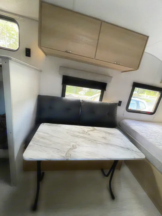 Compact rv rental interior featuring a marble-look dining table, dark cushions, and an adjacent bed. Ideal for road trips.. Forest River Salem 2024