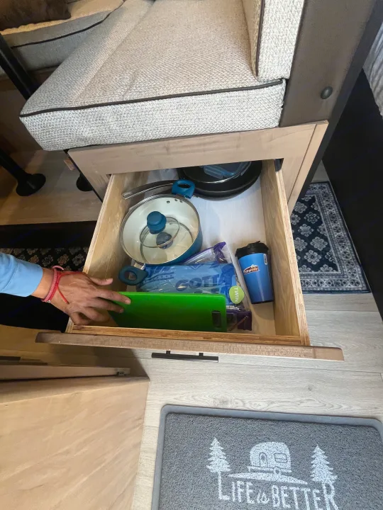 RV rental interior shows smart storage: an open drawer under seating holds compact kitchenware like a pot and cutting board.. Forest River Cherokee Cherokee Black Label 2025