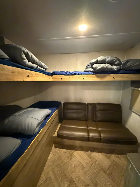 RV rental bunk beds & brown sofa in a compact interior, offering sleeping and lounge space.. Forest River Palomino Puma 2022
