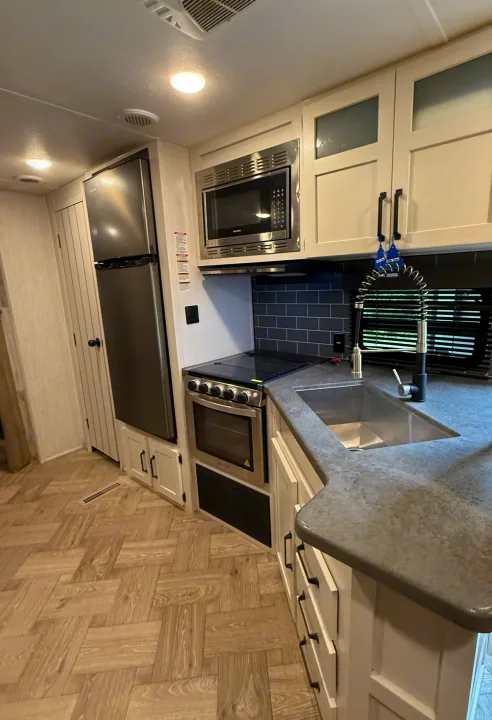 Modern RV rental kitchen features stainless steel appliances, dark countertops, and light cabinetry.. Forest River Palomino Puma 2022
