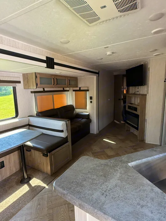 Bright RV rental interior: cozy dinette, comfortable sofa, kitchen counter, and entertainment center with TV & fireplace.. Forest River Palomino Puma 2022