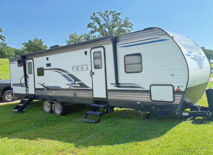A white and gray Puma travel trailer, ready as an RV rental, is parked on bright green grass on a sunny day.. Forest River Palomino Puma 2022