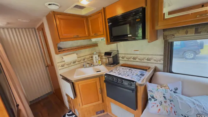 This RV rental features a well-equipped kitchen with a sink, stove, microwave, cabinets, and a cozy seating area.. Tioga FTWD 2004
