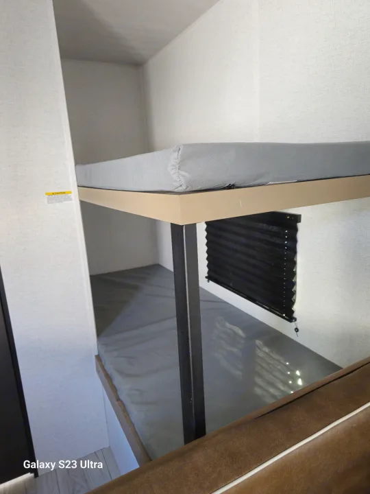 RV rental bunk beds with grey mattresses and a window blind. Perfect sleeping area for an RV interior.. Keystone RV Springdale 2025