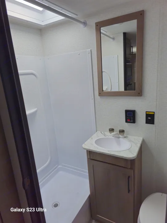 This RV rental bathroom features a compact shower stall, sink vanity, mirror, and toilet, ready for your travels.. Keystone RV Springdale 2025