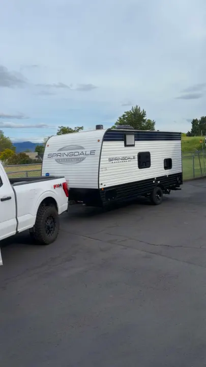 White pickup truck hitched to a modern white & black travel trailer. Ideal rv rental for camping & travel adventures.. Keystone RV Springdale 2025