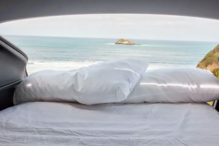 A clean white bed inside an RV rental offers a perfect ocean view with a distant island.. Telstar Model Y 2023
