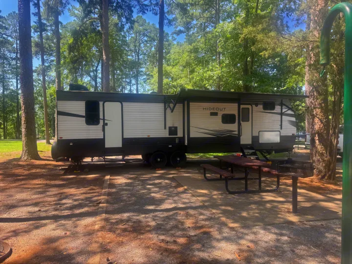 RV rental parked at a shady campsite with a picnic table and grill. Ideal for a nature getaway.. Keystone Hideout 2021