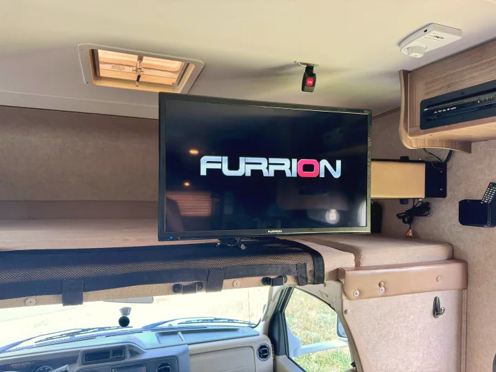 Inside an RV rental: a Furrion TV displays its logo, with a cozy bunk and entertainment system in the overhead cab area.. Coachmen Freelander 21QB 2016
