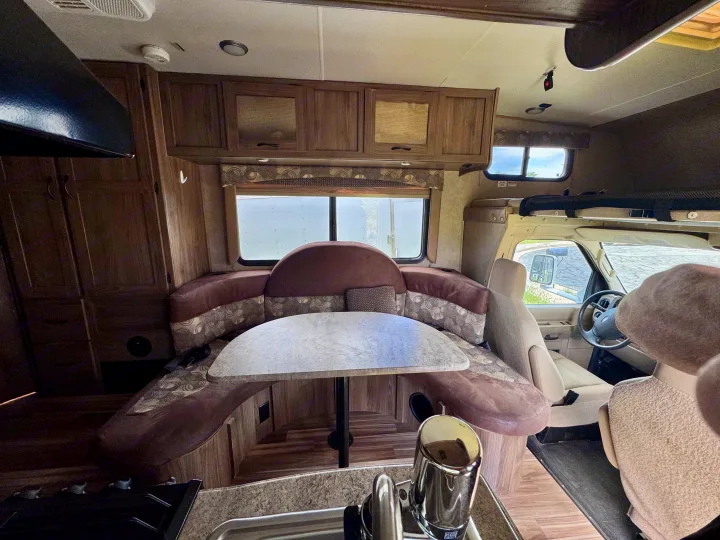 Spacious RV rental interior featuring a comfortable U-shaped dinette, kitchen counter, and overhead cabinets near the driver's cabin.. Coachmen Freelander 21QB 2016