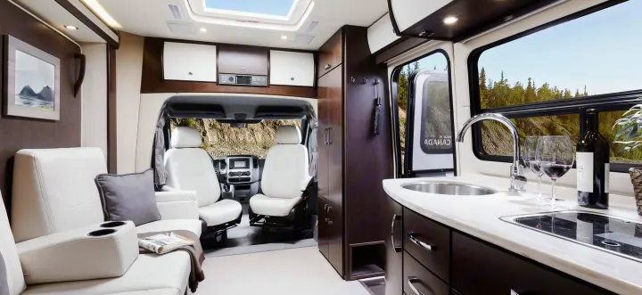 Spacious rv rental interior with living area, white driver's seats, and a modern kitchenette with wine, perfect for a scenic trip.. Leisure Travel Vans Unity 2016