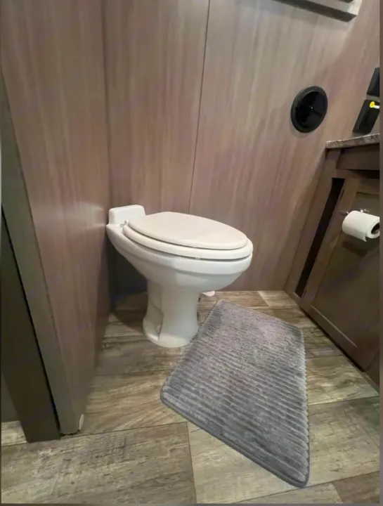 RV rental bathroom features: white toilet, wood-look walls, gray mat, and wall vent. Compact comfort.. Crossroads RV Sunset Trail Super Lite 2022