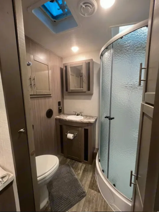 RV rental: bright, compact bathroom featuring a toilet, vanity, and curved glass shower. Functional wood-look interior.. Crossroads RV Sunset Trail Super Lite 2022