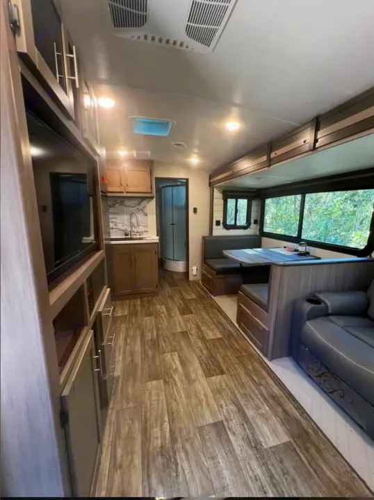 An inviting RV rental interior showing a modern kitchen, dining booth, and entertainment center in the living area.. Crossroads RV Sunset Trail Super Lite 2022