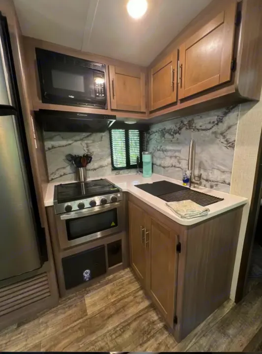 Well-equipped RV rental kitchen featuring a microwave, stove, sink, and marbled backsplash.. Crossroads RV Sunset Trail Super Lite 2022