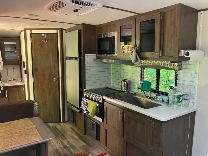 RV rental interior featuring a modern kitchen with stove, microwave, sink, and fridge, plus dining area and wooden accents.. Riverside RV Retro 2021